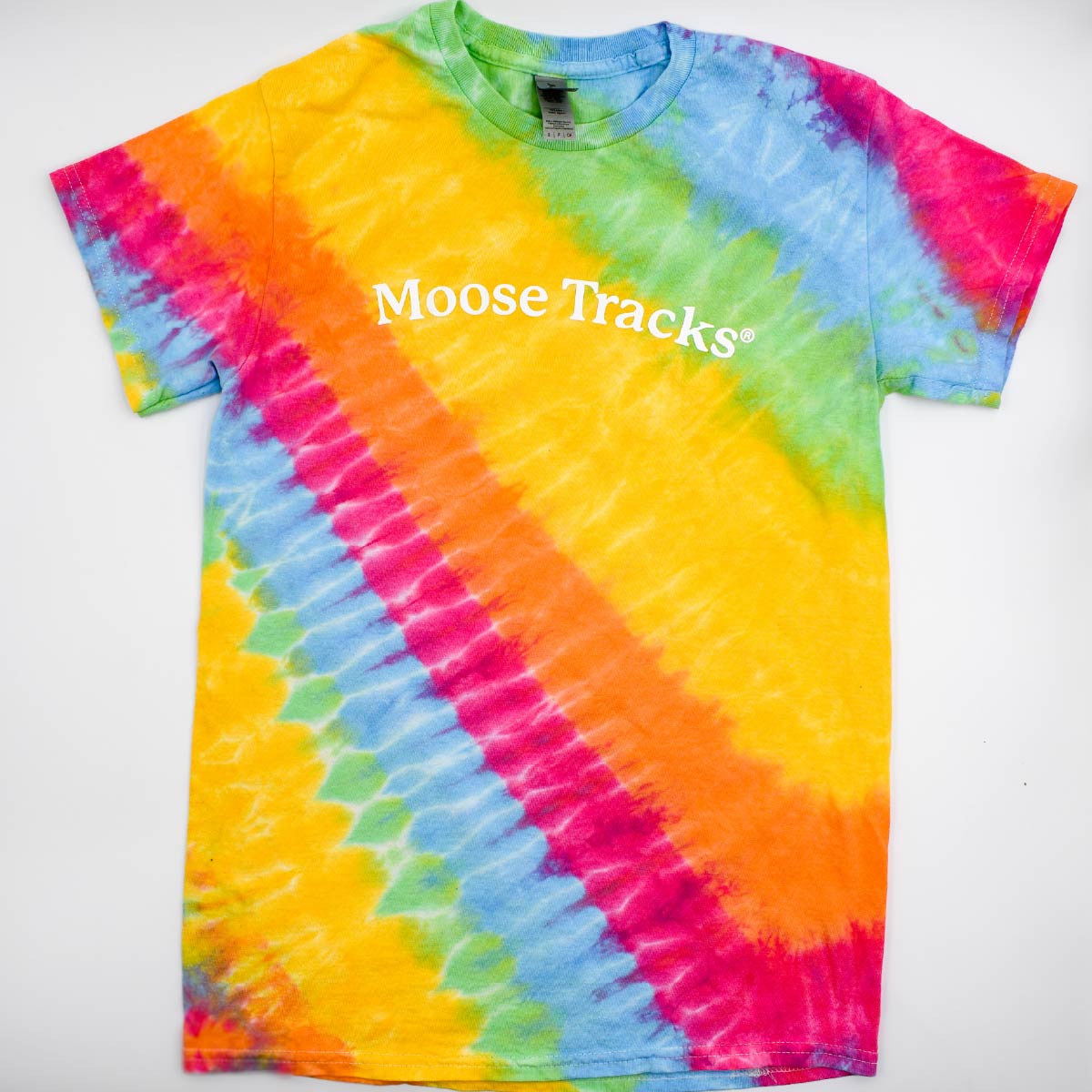An aerial view of the Moose Tracks Tie-Dye T-Shirt laying on a flat surface. The shirt features a rainbow pastel tie-dye pattern with white screen-printed text in the center that reads "Moose Tracks".