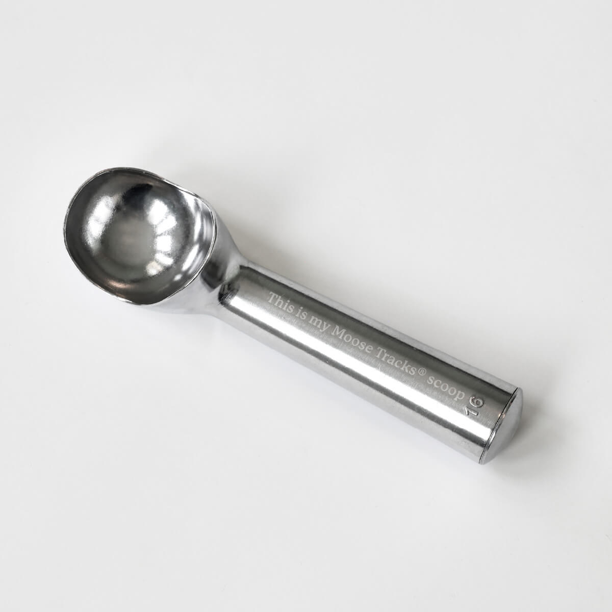 An aluminum ice cream scoop sitting on a white surface with laser-engraving on the handle that reads, "This is my Moose Tracks scoop".