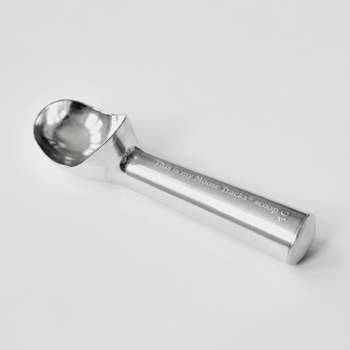 An aluminum ice cream scoop sitting on a white surface with laser-engraving on the handle that reads, "This is my Moose Tracks scoop".