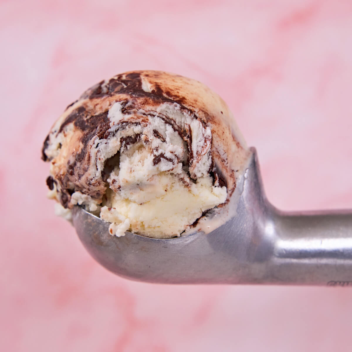 An aluminum ice cream scoop against a marble pink surface, with a scoop of Moose Tracks ice cream in it.