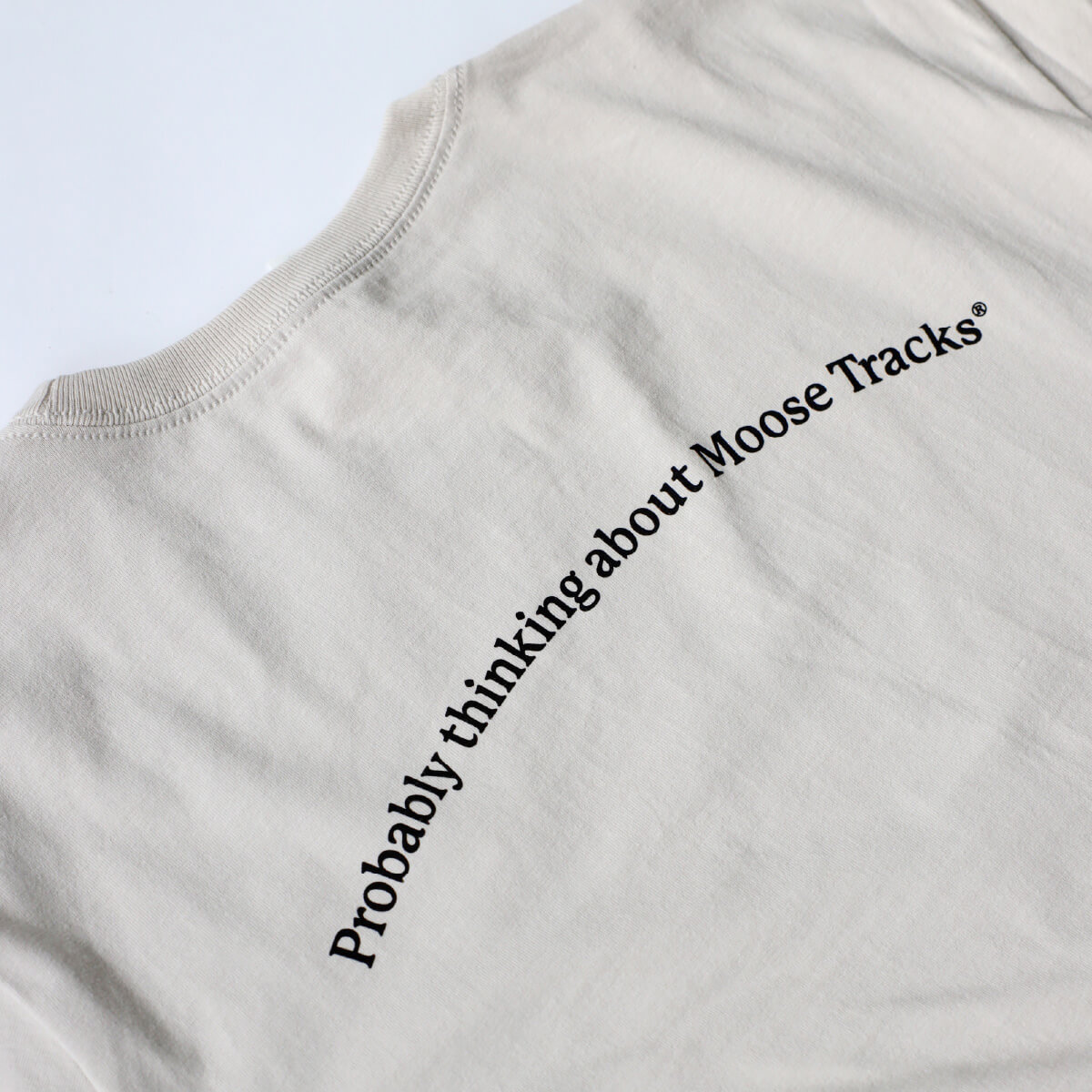 A close-up of a light-colored t-shirt featuring text that reads, "Probably thinking about Moose Tracks" on the back.