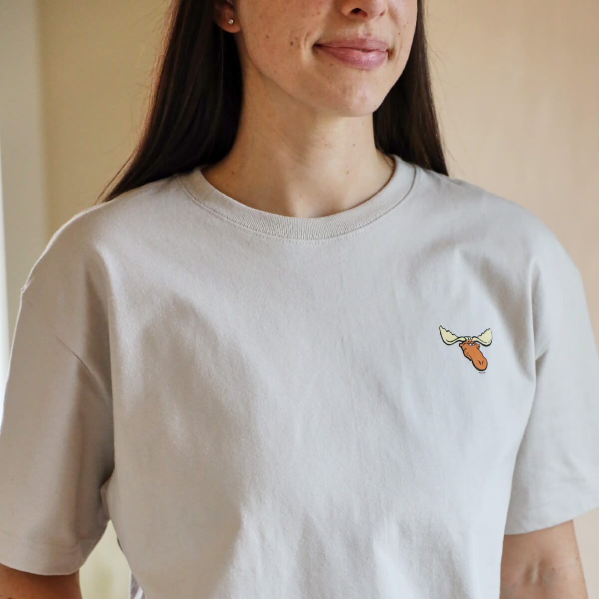 A woman wearing a light-colored t-shirt featuring a moose head logo on the left chest.